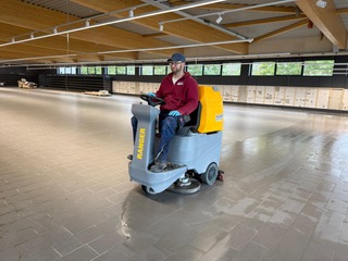 Ein Mitarbeiter der Herdegen Gebäudeservice GmbH reinigt mit einer professionellen Aufsitz-Scheuersaugmaschine großflächige Bodenbereiche in einer Gewerbehalle.